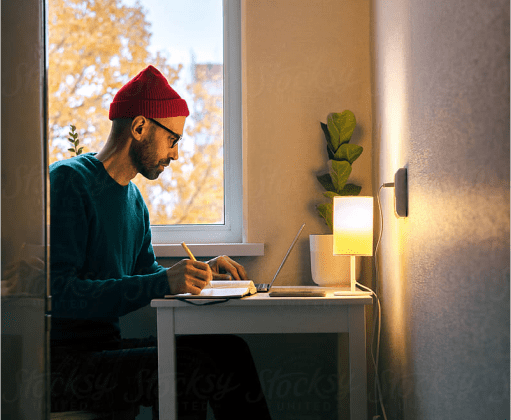 A man sitting at a desk in front of a laptop while writing in a journal