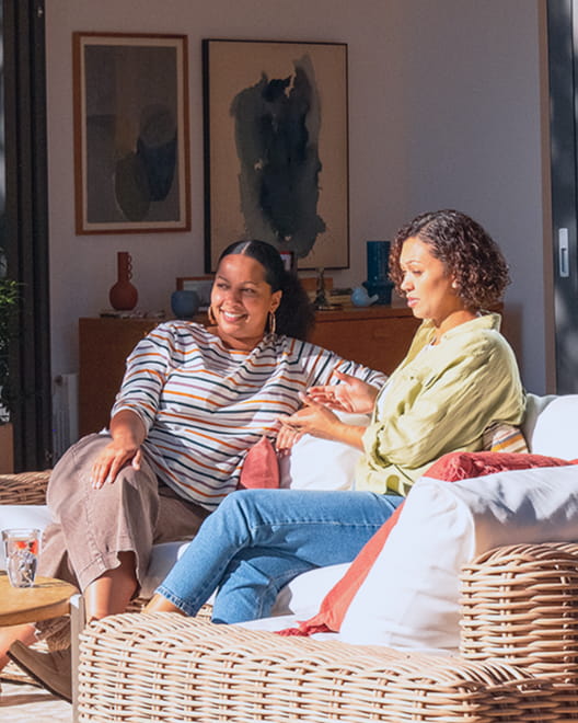 Two women talk while relaxing on a sun-filled patio.