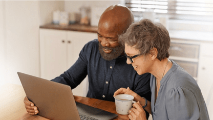 A man and a woman sitting at a table while looking at a laptop