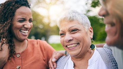 A group of women smiling while gathered together in a park.