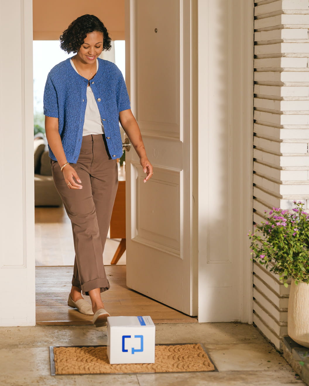 A woman picks up a Cologuard Plus box that’s just been delivered to her door.