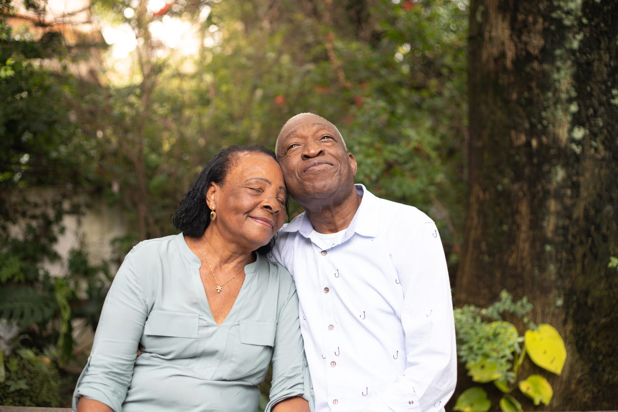  An older couple in a wooded setting, gently leaning into each other.