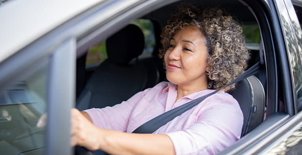 Una mujer con una agradable expresión en su rostro está tras el volante de un auto.