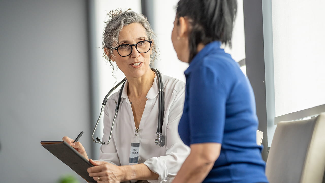 Un médico sosteniendo un expediente médico está hablando con su paciente.