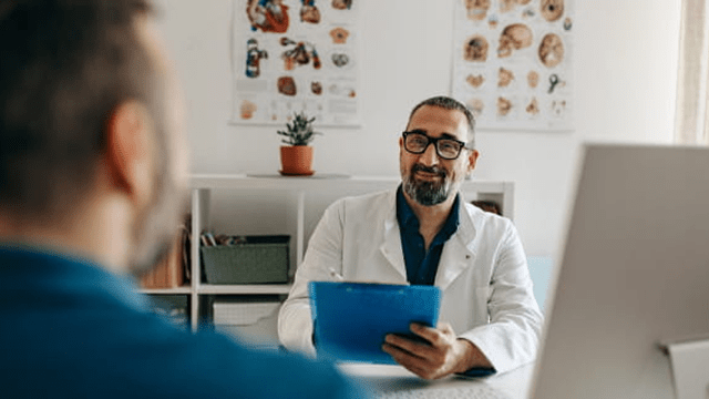 Un médico sosteniendo un expediente médico está hablando con su paciente.